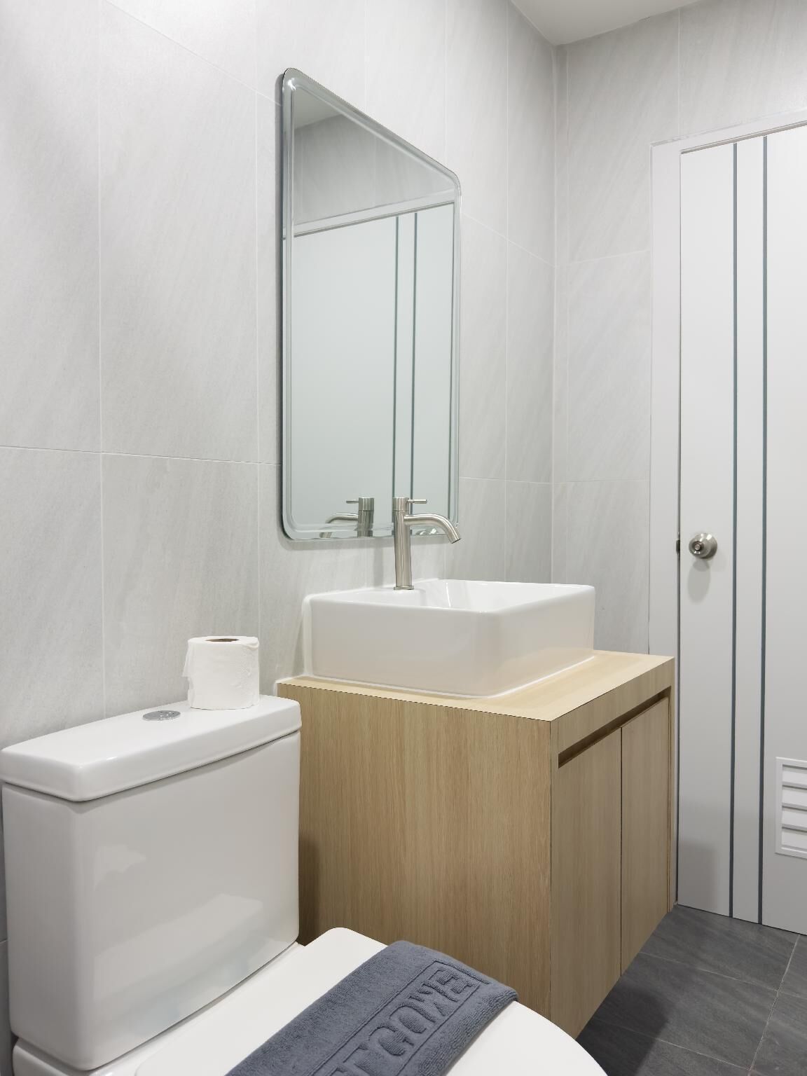 Un baño moderno con inodoro, lavamanos, espejo y una toalla en el suelo.