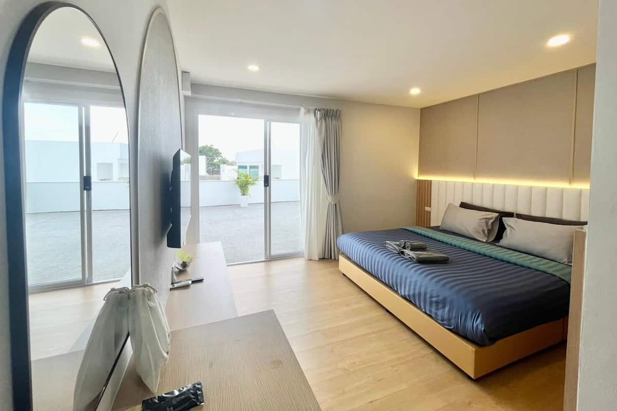 Quarto de hotel moderno com uma cama grande, uma mesa com cadeira, uma TV de tela plana e uma grande janela com vista para o exterior.