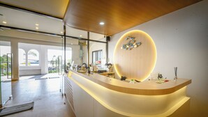 A modern reception desk with a wooden finish and a circular light fixture above it. - Ti amo Kohlarn (Koh Lan)