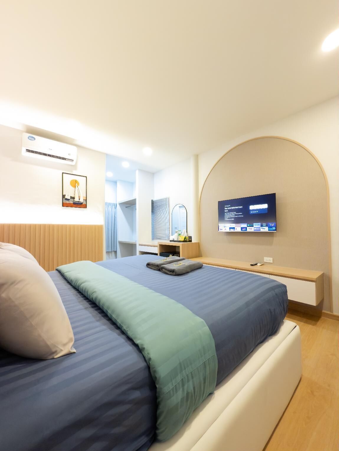 A modern hotel room with a bed, a TV, an air conditioner, and a desk with a mirror.