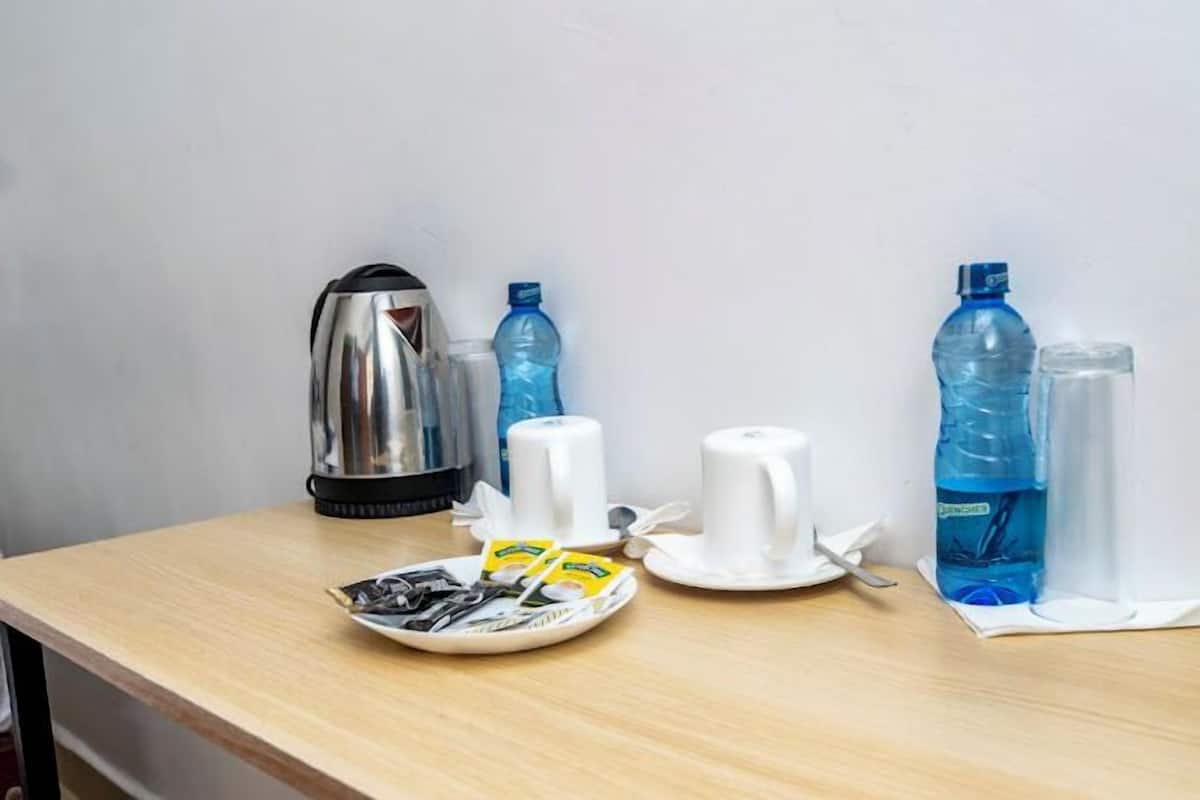 Una preparación para el desayuno con una tetera, dos botellas de agua, un plato con sobres de café instantáneo y dos tazas blancas sobre una mesa de madera.