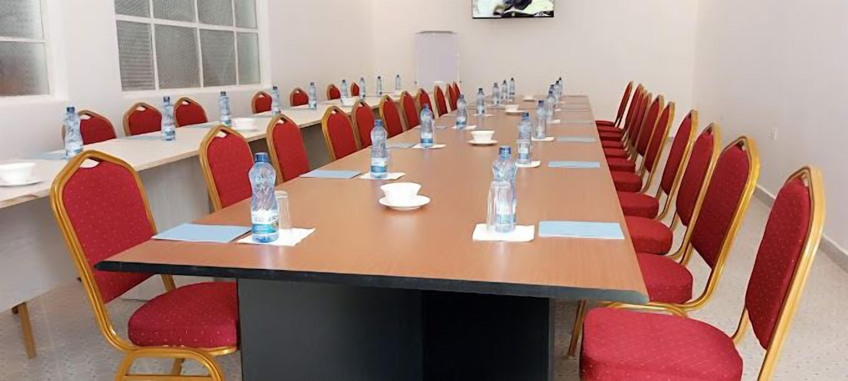 Ein Konferenzraum mit einem langen Tisch, roten Stühlen und Wasserflaschen an jedem Platz.