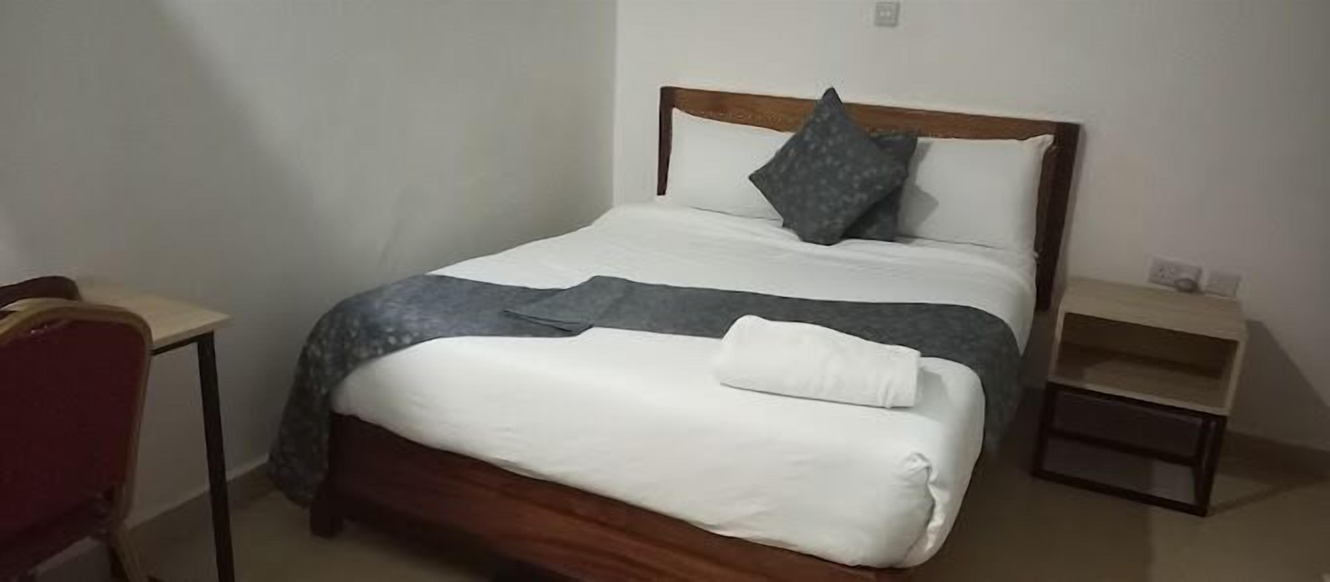 Una cama bien hecha con cabecera de madera, una manta gris y un almohadón blanco.