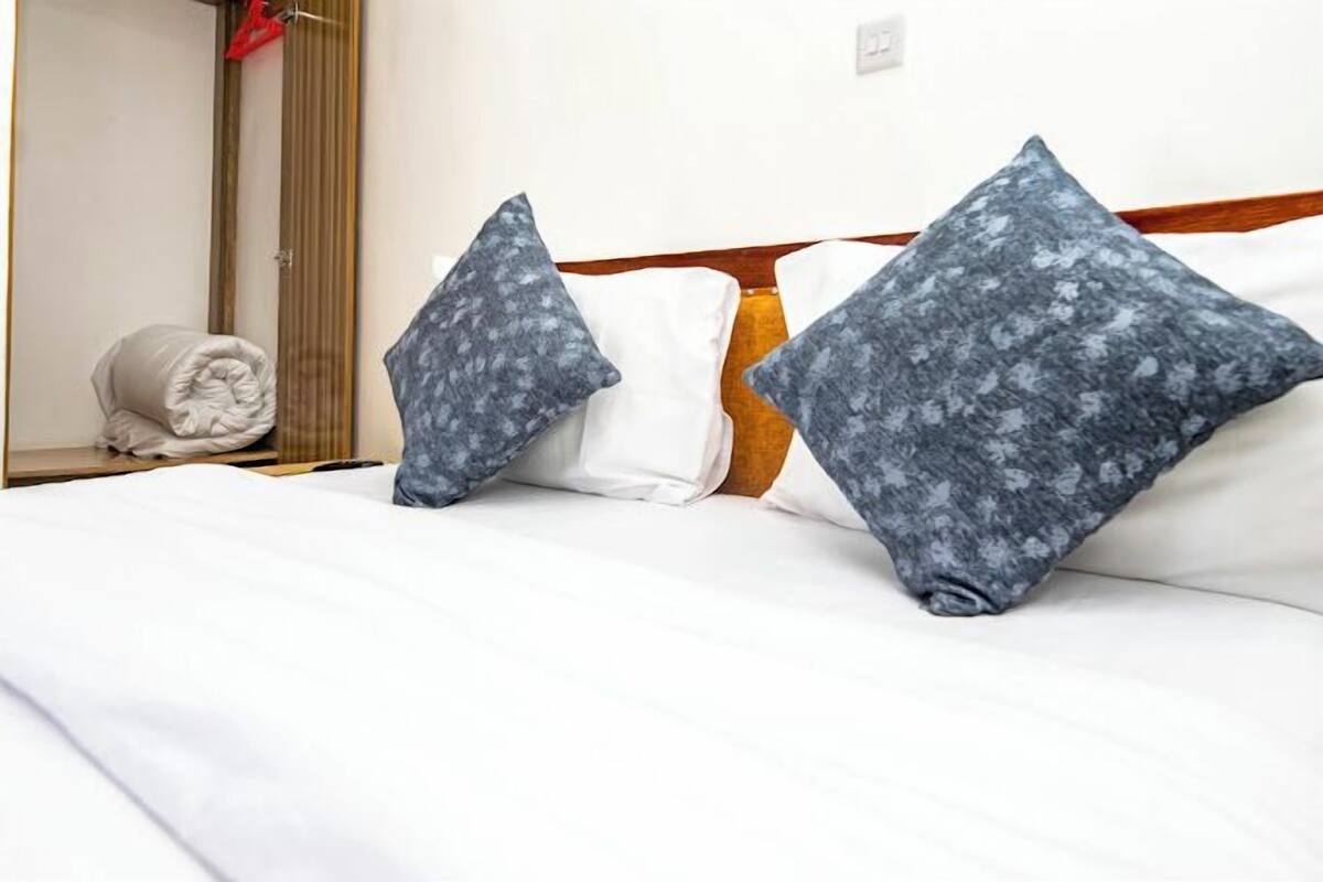 Habitación de hotel con una cama bien hecha, dos almohadas, una toalla enrollada y un cabecero de madera.