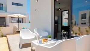 Un espace extérieur moderne aménagé avec des chaises blanches et une table où sont disposées des boissons et des collations.