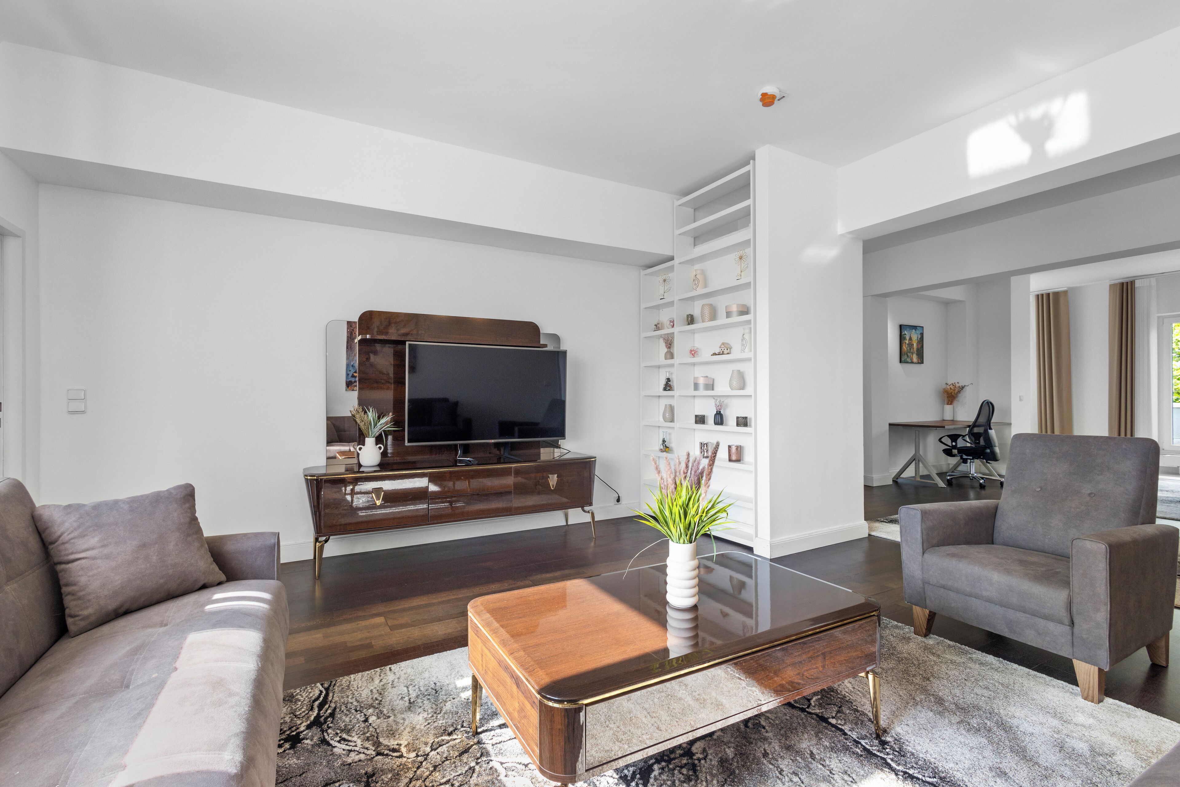 Ein modernes Wohnzimmer mit Sofa, Sesseln, Couchtisch, Fernseher und Einbauschränken.