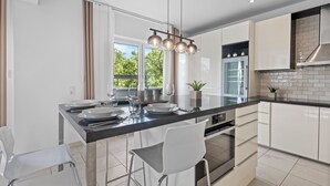 A modern kitchen with a central island, white cabinetry, stainless steel appliances, and a pendant light fixture. - Domloge Lofts & Apartments (Cologne)