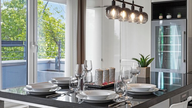 A modern kitchen with a glass island, stainless steel appliances, and a view of greenery outside. - Domloge Lofts & Apartments (Cologne)