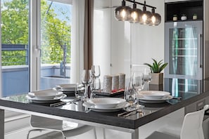 Une cuisine moderne dotée d’un îlot central en verre, d’appareils électroménagers en acier inoxydable et offrant une vue sur la verdure environnante.