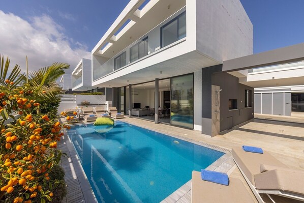 Una casa moderna con piscina, mobiliario exterior y balcón.