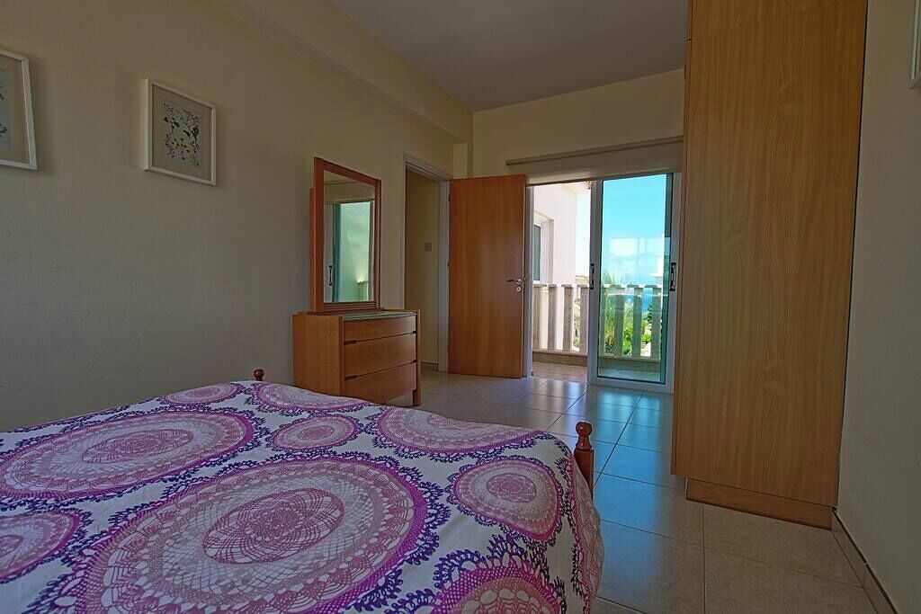Un dormitorio con cama, cómoda y un espejo grande. Hay una puerta corrediza de vidrio que da a un balcón.