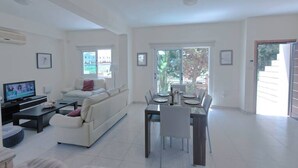 Un salón amplio con sofá, mesa de centro, televisor y mesa de comedor con sillas.