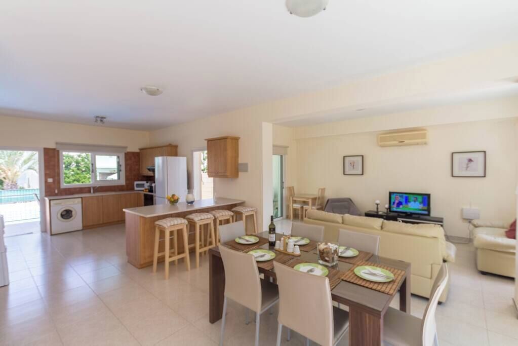 A modern kitchen with a dining area, a living room with a sofa, and a television.