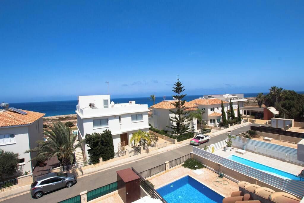 A residential area with a swimming pool, a view of the sea, and a street with parked cars.