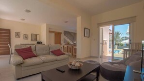 Una sala de estar con un sofá, una mesa de centro y un televisor. Se ve una escalera que lleva a otra habitación.
