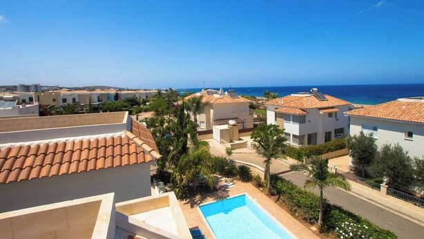 Zona residencial con piscina, tejados de tejas rojas y vista al mar.
