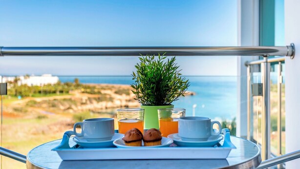 Un balcon avec un plateau de mets pour le petit-déjeuner, une plante en pot et une vue sur la mer.