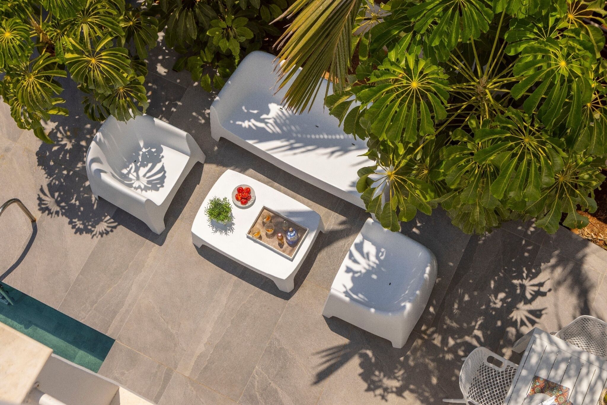 An outdoor seating area with white chairs and a table, surrounded by lush green foliage.