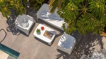 An outdoor seating area with white chairs and a table, surrounded by lush green foliage.