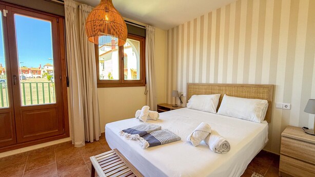 A hotel room with a large bed, a wooden bench, a hanging light fixture, a window with curtains, and a striped wall.