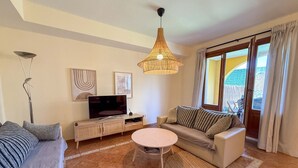 A living room with a sofa, a coffee table, a TV, and a wicker pendant light.
