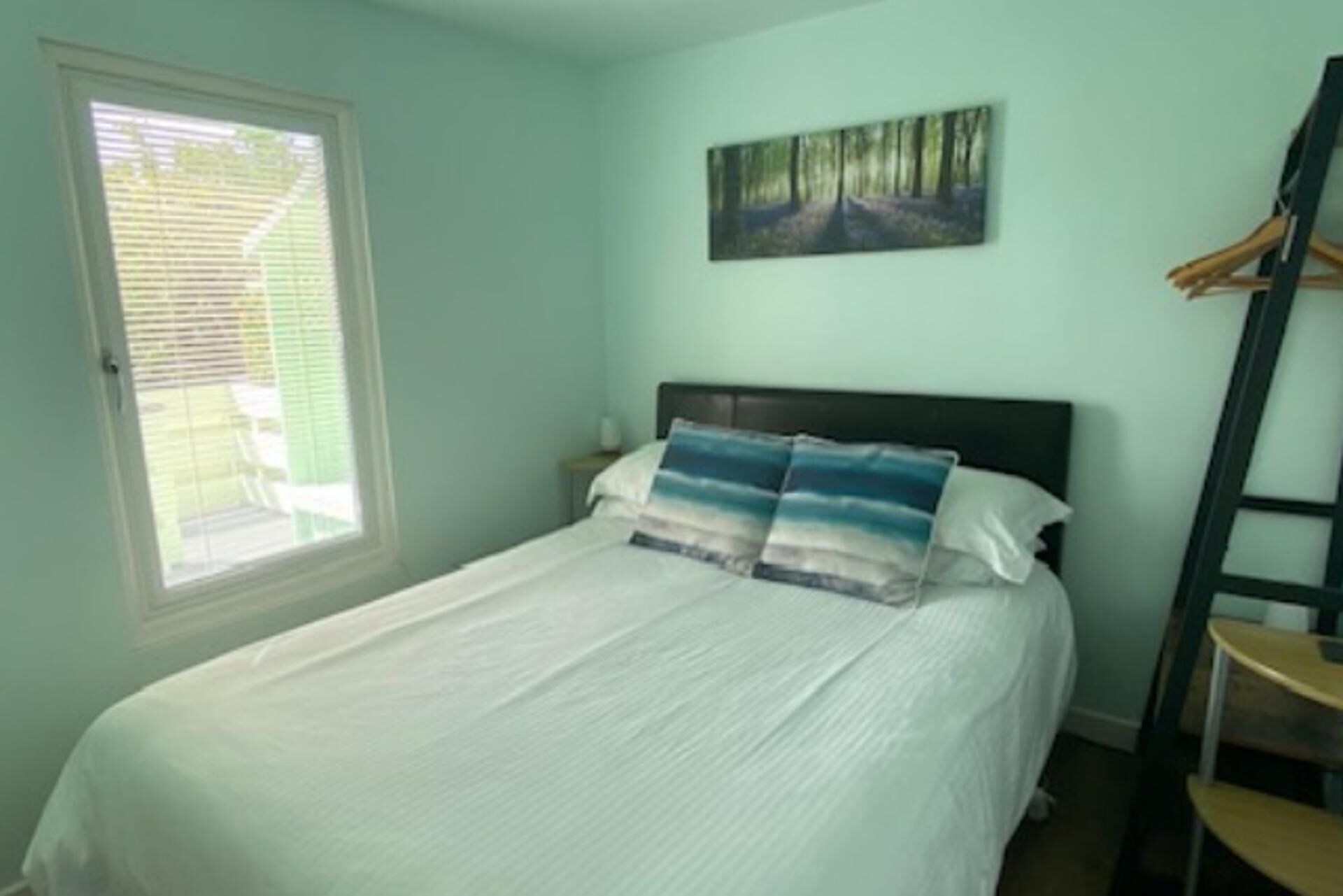 A bedroom with a bed, a window, a painting, and a wooden chair.