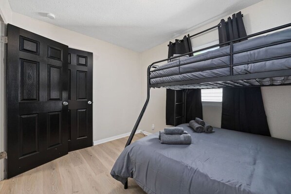 A room with a bunk bed, a dark wooden door, and a window with curtains.