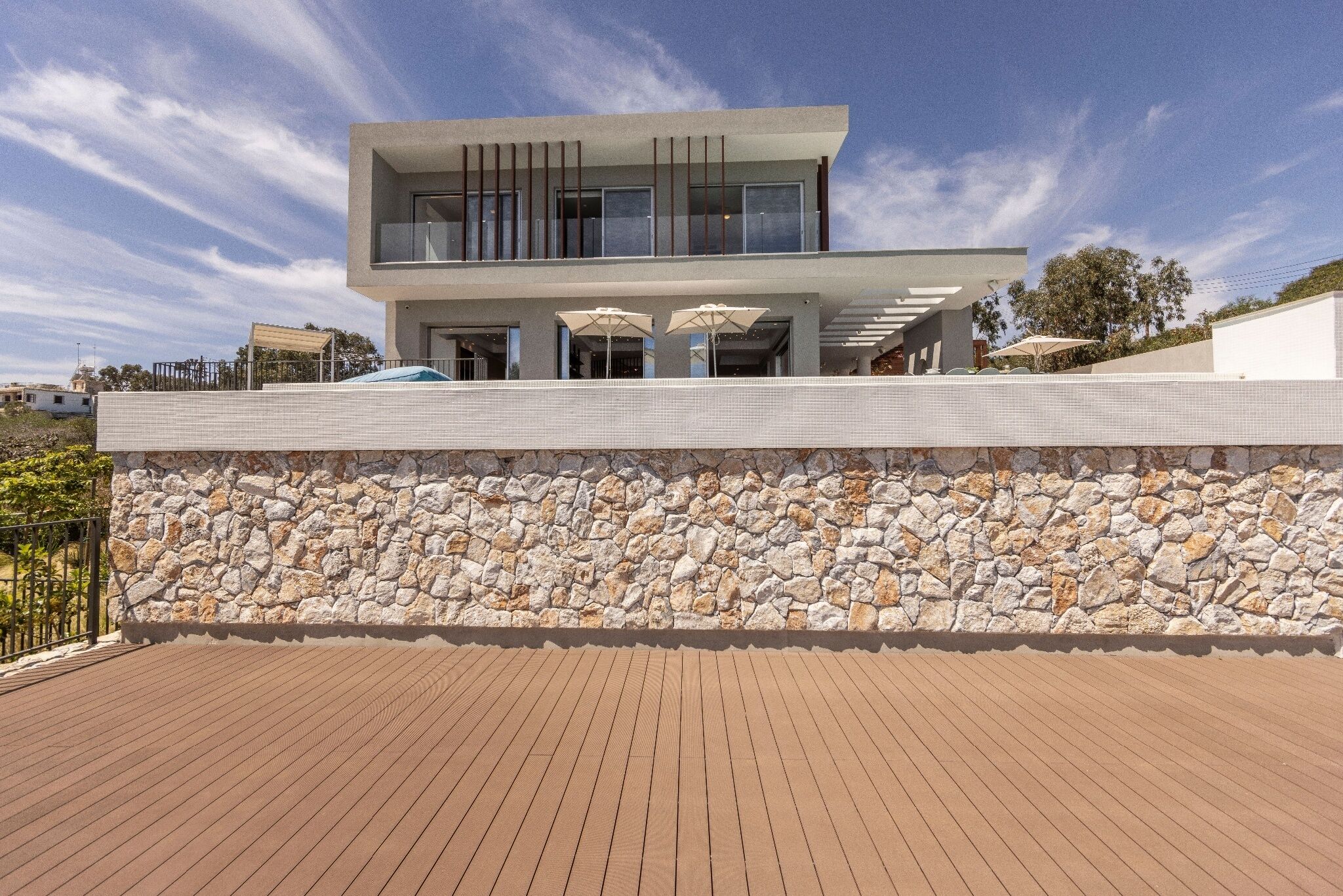 A modern house with a stone wall and a wooden deck.