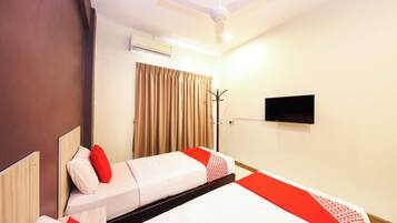 A hotel room with two beds, a ceiling fan, an air conditioning unit, a TV mounted on the wall, and a window with curtains.