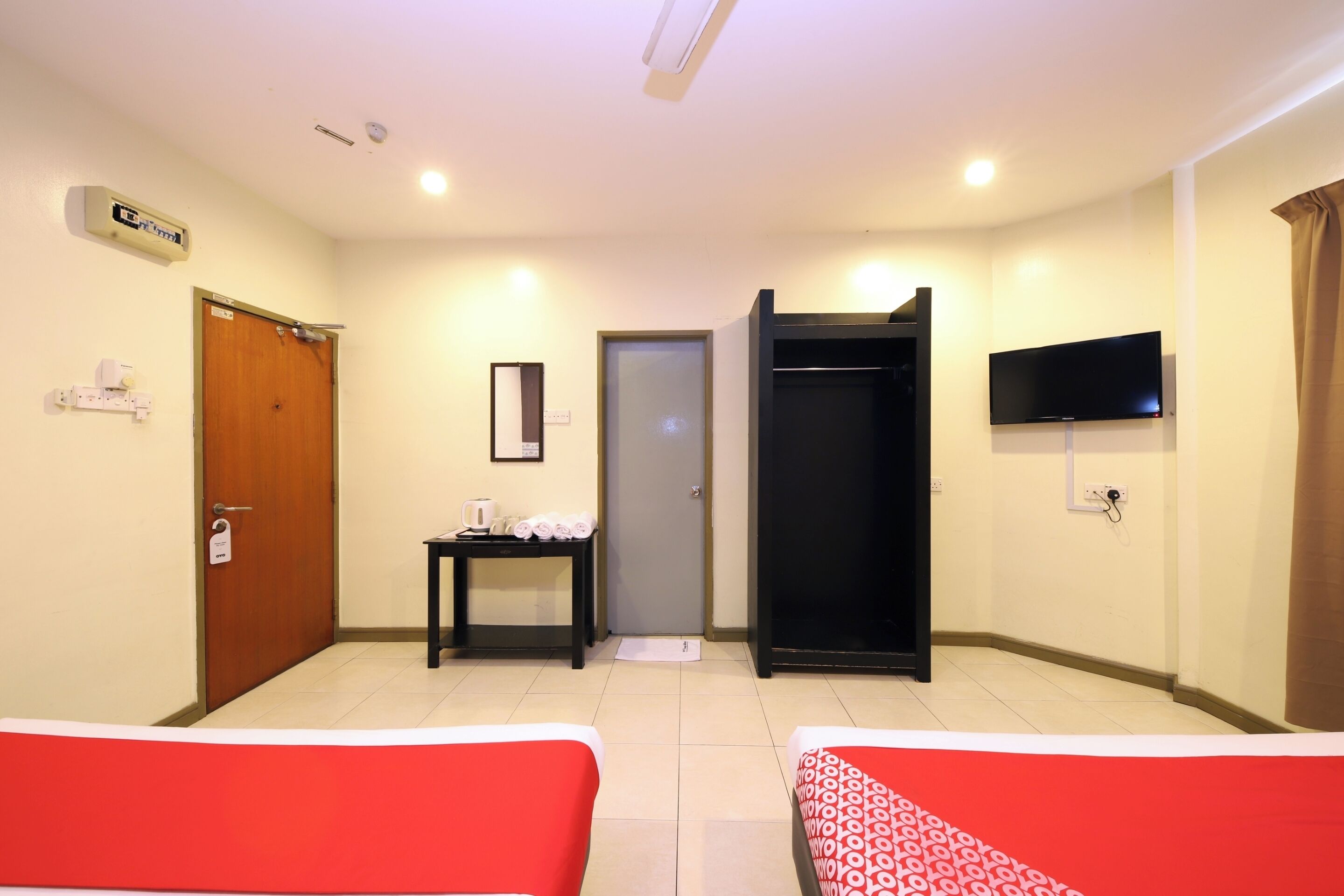 A hotel room with two beds, a desk with a kettle and towels, a wardrobe, a television, and a door with a sign.