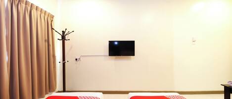 Habitación de hotel con dos camas, un televisor de pantalla plana en la pared y un perchero.