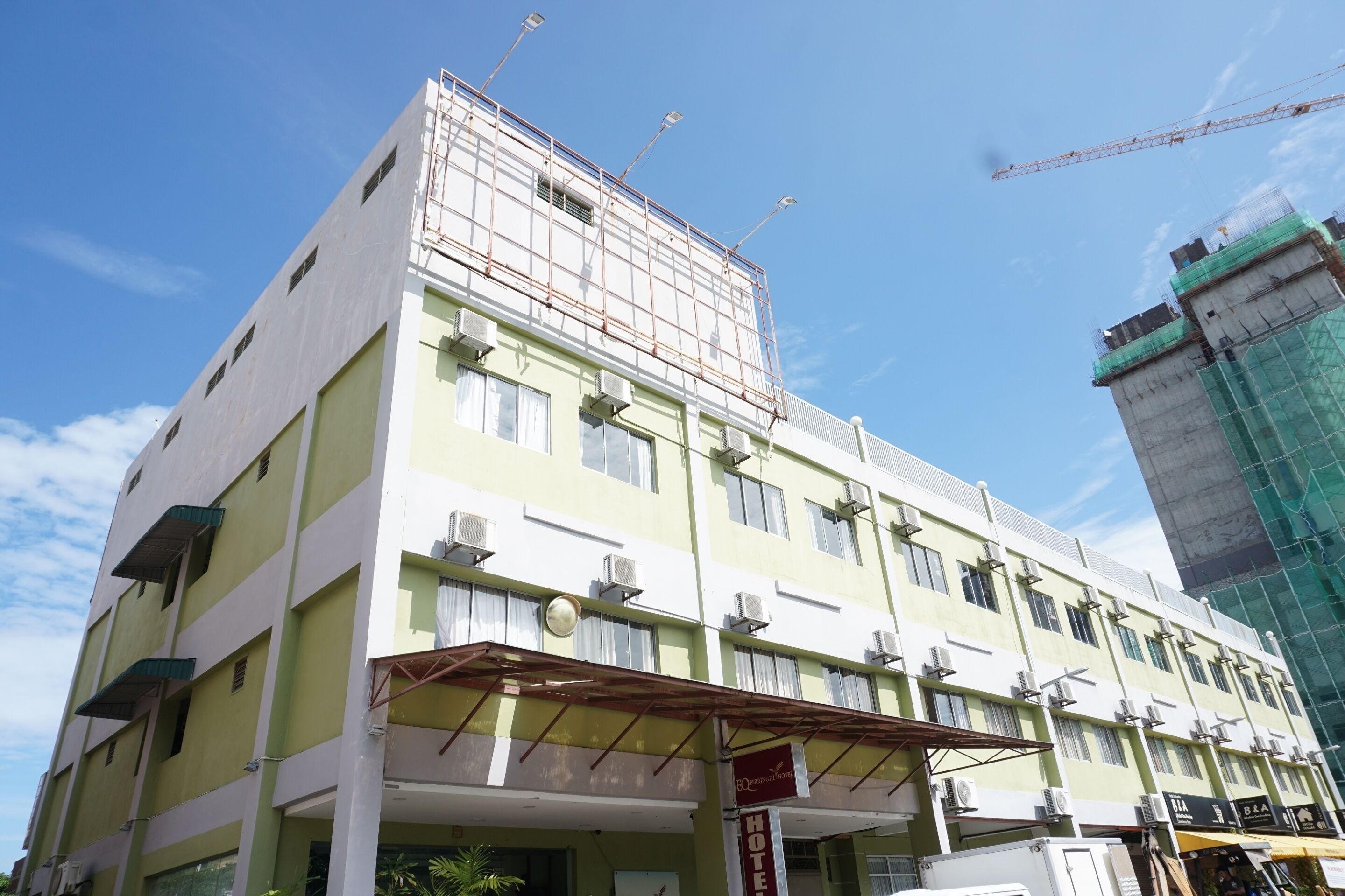 A multi-story hotel with a green facade, multiple balconies, and a construction crane in the background.