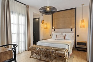 A bedroom with a large bed, bedside tables, a wicker bench, and a hanging light fixture.