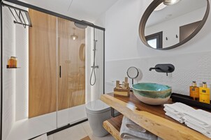 Een moderne badkamer met een douchecabine van hout, een grote spiegel en een houten wastafelmeubel met een wasbak.