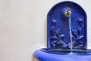 Una fuente azul con agua brotando de un chorro central, rodeada de detalles florales.