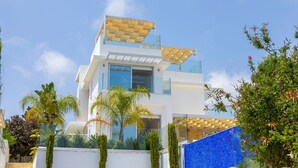 A modern two-story building with a glass facade, solar panels on the roof, and a blue-tiled wall. - Milos lifestyle 5 bedroom villa (Protaras)