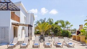 A pool area with lounge chairs, a pergola, and a barbecue area.
