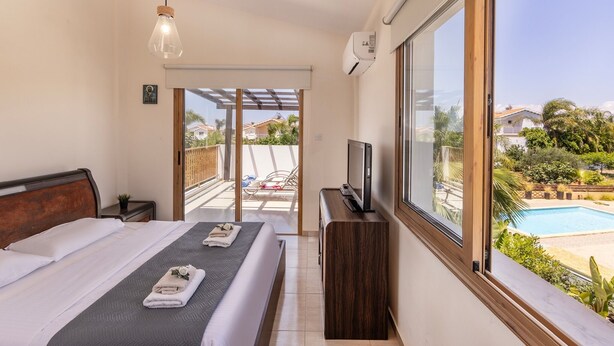 A modern hotel room with a large bed, a TV, and a view of a swimming pool.