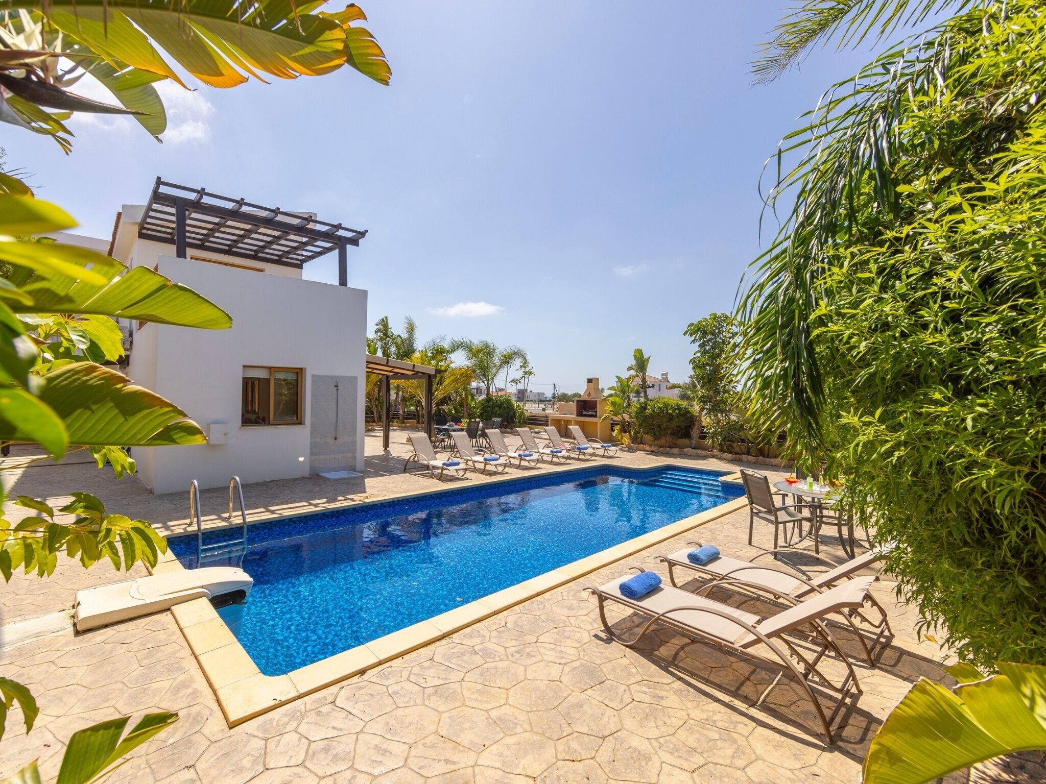 Une piscine avec des chaises longues, une pergola et un bâtiment moderne à la façade blanche.
