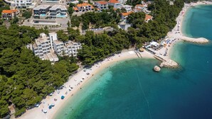 Vista aérea de una zona costera con playa, edificios y un promontorio rocoso.