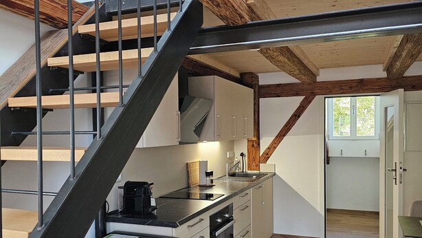 Eine moderne Küche mit einer Holztreppe, Einbaugeräten und Blick auf den oberen Stock.