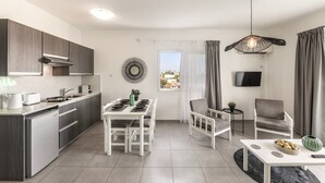 A modern apartment with a kitchen, dining area, and living space. It includes a dining table with chairs, a sofa, a TV, and a ceiling light fixture. - 1 bedroom apartment heart of Protaras (Protaras)