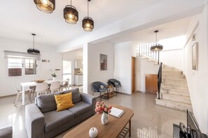 Ein modernes Wohnzimmer mit einem grauen Sofa, einem Holztisch und einer Blumenvase. Eine Treppe führt nach oben.