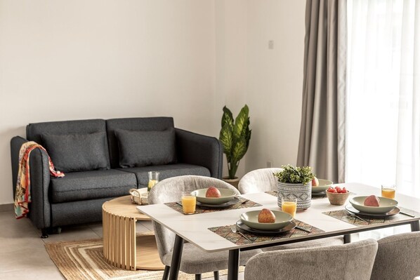 Ein modernes Wohnzimmer mit einem dunkelgrauen Sofa, einem Esstisch mit Tellern, Gläsern und einer Pflanze.