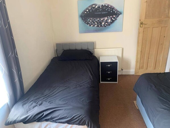A bedroom with a single bed, a dresser, a radiator, and a door. - By the Sea, Sleeps 4-6, Private Patio, Nearbeach, Seasideretreat, Train to Liverpool or Chester is a hop Skip and a Jump Away (Wirral)