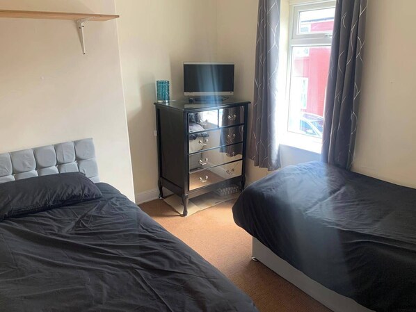 A bedroom with two beds, a dresser, a television, and a window with curtains. - By the Sea, Sleeps 4-6, Private Patio, Nearbeach, Seasideretreat, Train to Liverpool or Chester is a hop Skip and a Jump Away (Wirral)