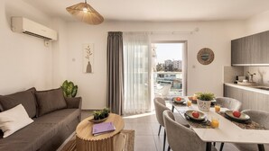 A modern living room with a sofa, dining table, and chairs. There is a balcony with a view of buildings.