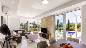 A modern living room with a sofa, chairs, a dining table with fruit, a TV, and a stone wall. - Discover your perfect getaway at this stunning 3-bedroom villa in Cape Greko, Famagusta, Cyprus. (Protaras)