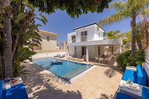 A poolside area with a swimming pool, lounge chairs, and a dining table with a tray of drinks. - 2 Bedroom Villa In The Center of Protaras (protaras)
