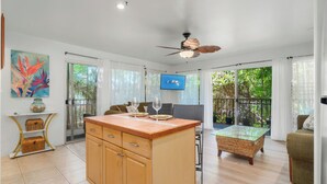 A spacious living area with a wooden cabinet, a glass coffee table, and a television mounted on the wall.